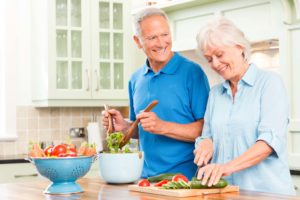 Cheerful senior couple preparing vegetable salad in kitchen. Horizontal shot.